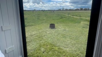 Een kamer met een groot raam met uitzicht op een grasveld en een bewolkte lucht.