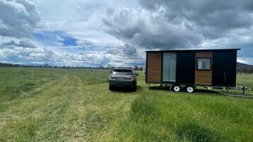 A small, modern mobile home with a trailer, parked in a grassy field with a car beside it.