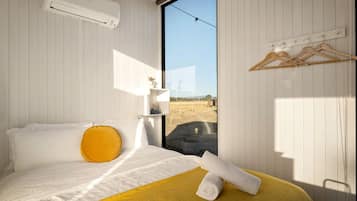 Een slaapkamer met een bed, een raam, een wandairconditioner en een houten kledingrek.