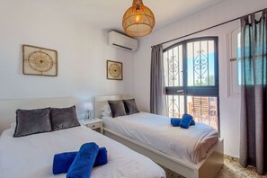 Ein Hotelzimmer mit zwei Betten, einem großen Fenster mit Vorhängen, einer Hängelampe und einer Wand-Klimaanlage.