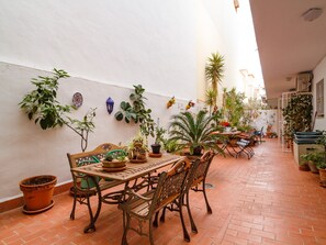 Eine Terrasse im Freien mit Terrakottafliesen, Holzmöbeln und verschiedenen Topfpflanzen.
