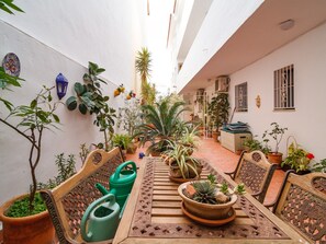 Eine Außenpatio mit einem Holztisch und Stühlen, umgeben von Blumentöpfen und einer weißen Wand.