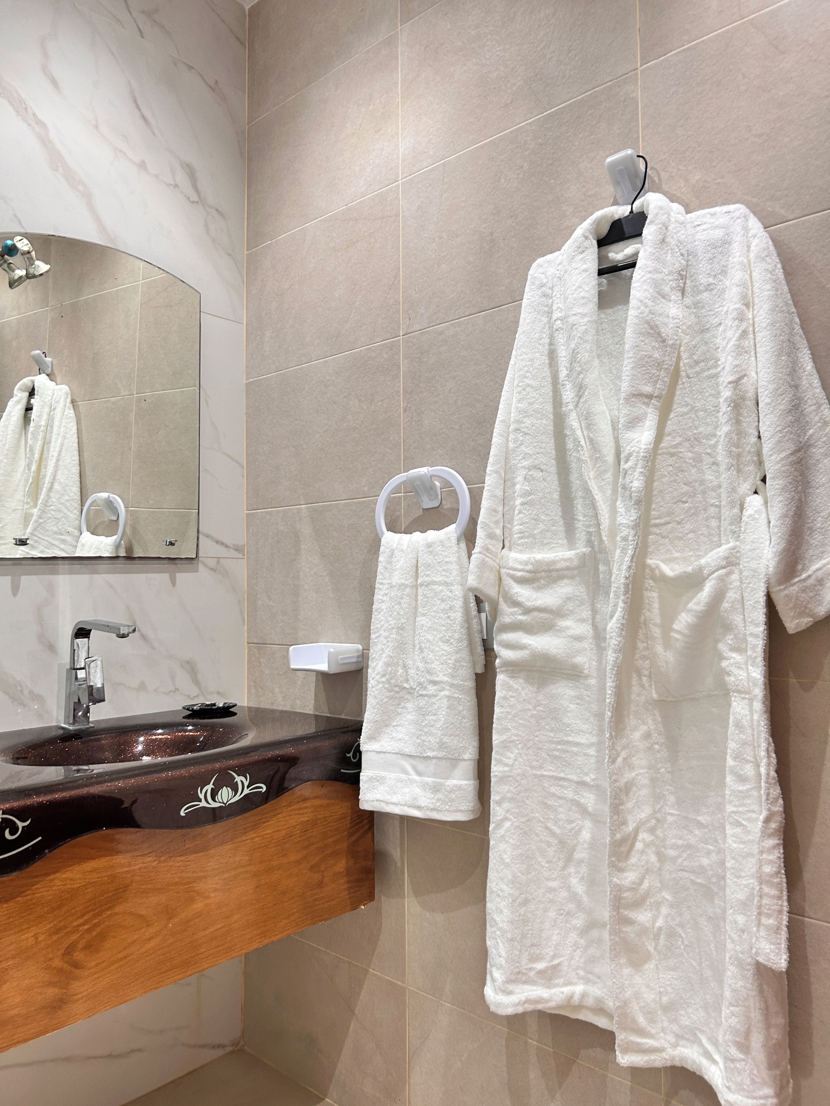 Une salle de bain avec un mur en marbre, un lavabo avec un meuble en bois et deux serviettes blanches suspendues à des crochets.