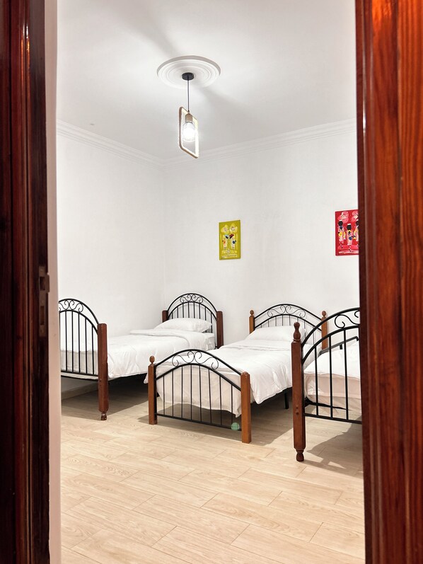 A room with three wooden beds, white walls, and a light fixture.