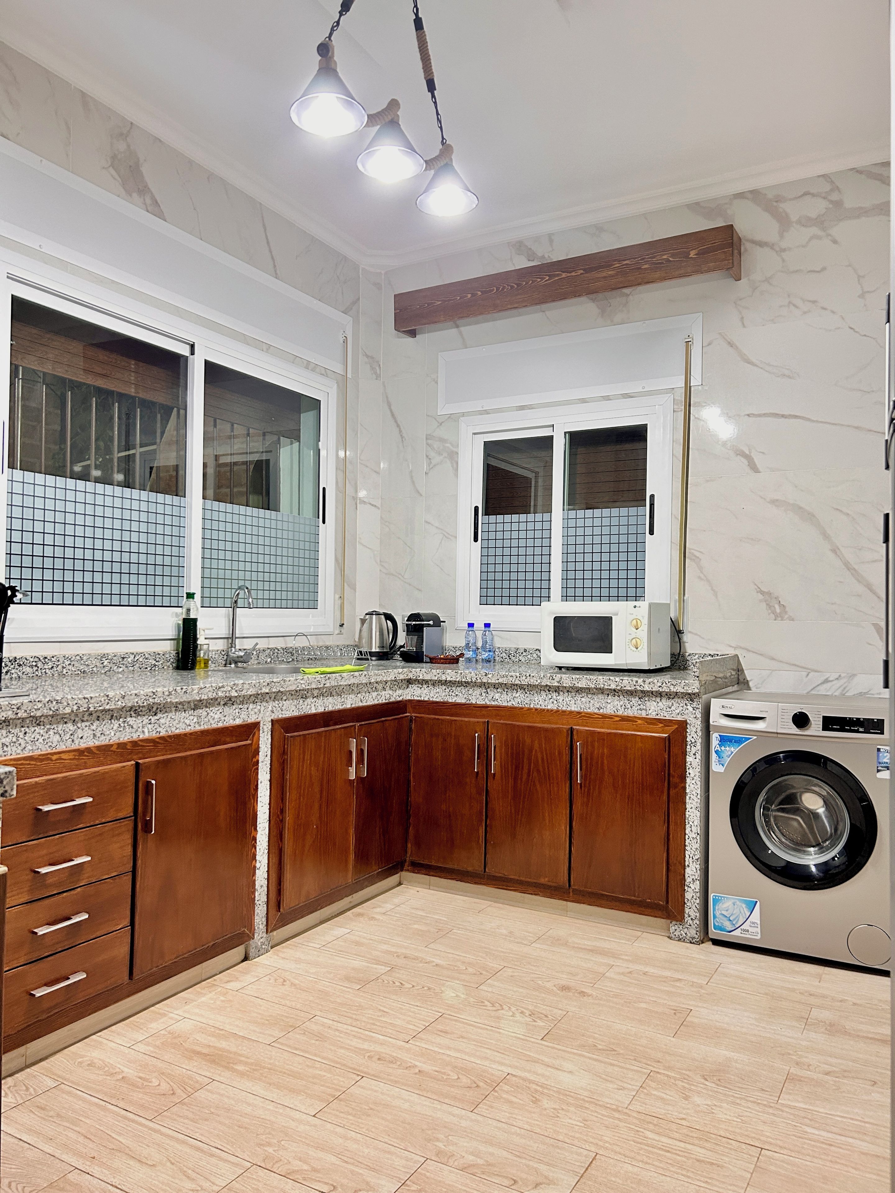 Une cuisine avec des meubles de rangement en bois, un four à micro-ondes encastré et un lave-linge.