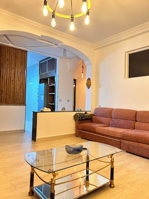Una sala de estar con una mesa de centro de vidrio, un sofá y una cocina al fondo.
