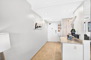 A hallway with a welcome sign, a door, a kitchen area with a countertop, and a potted plant. - New Luxury Retreat  Vast Ocean Views & Huge Lanai (Lahaina)