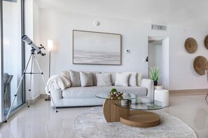 A modern living room with a white sofa, a glass coffee table, and a telescope on a tripod. - Beachfront Nirvana | Corner View • Pool • Gym (Hollywood)
