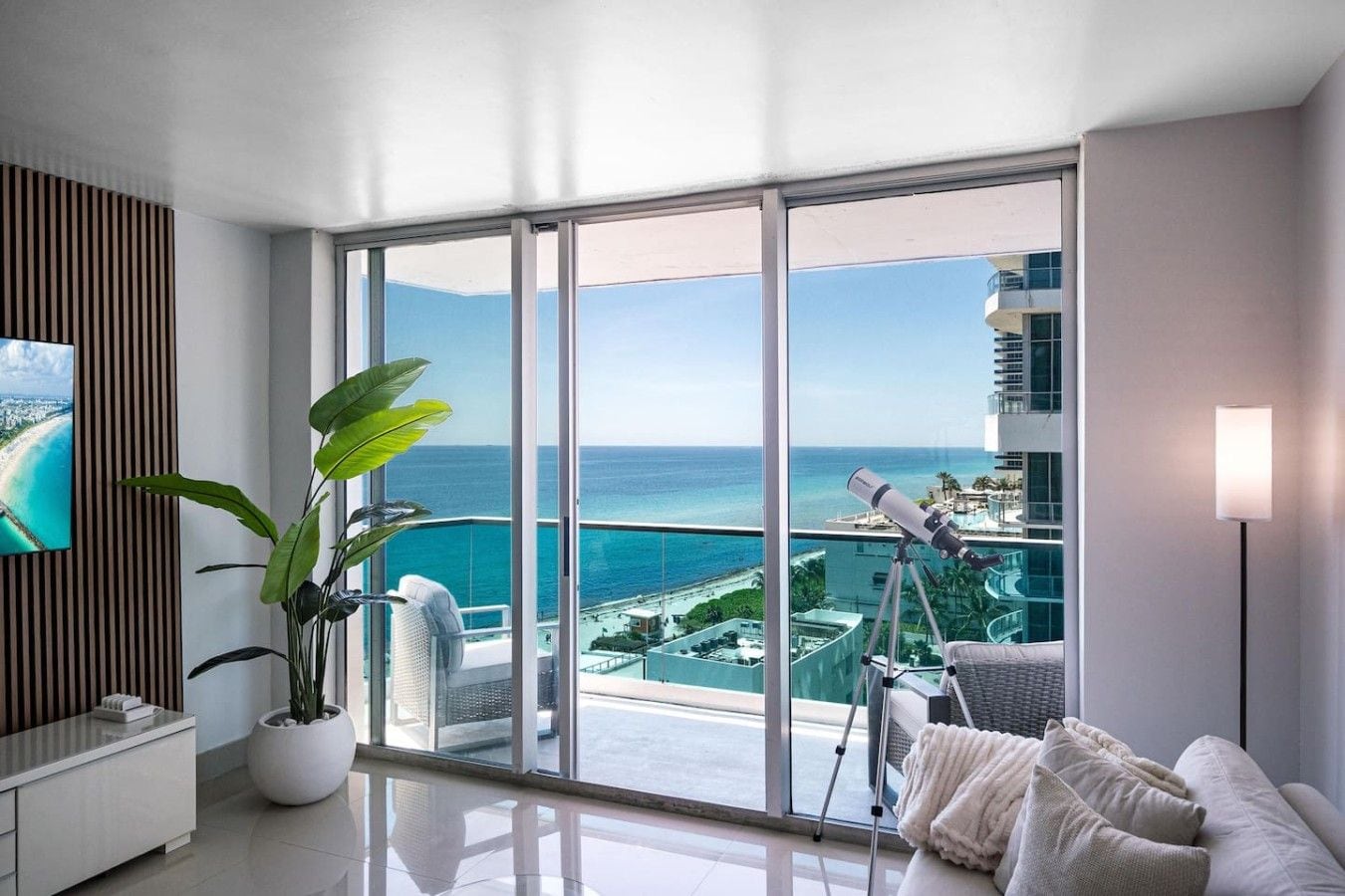 A modern living room with a large balcony, a telescope, and a TV on the wall.