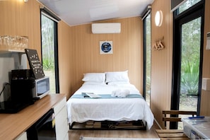 A compact room with a bed, a coffee machine, a small desk, and a window with a view of greenery.