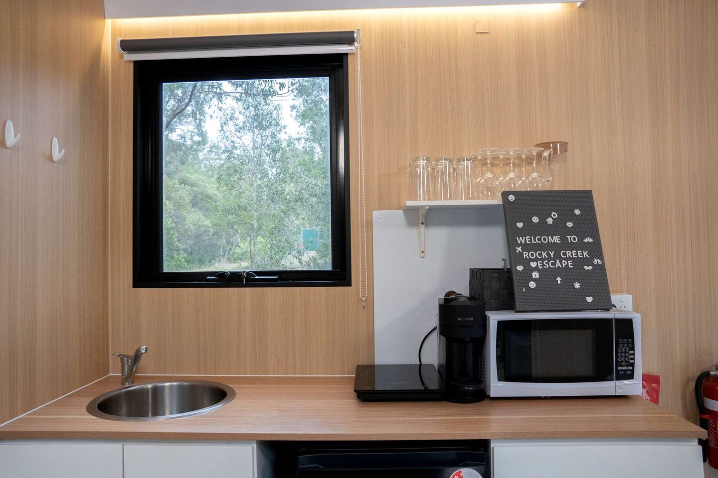 A compact kitchen with a window, a coffee maker, a microwave, and a sign on the counter.