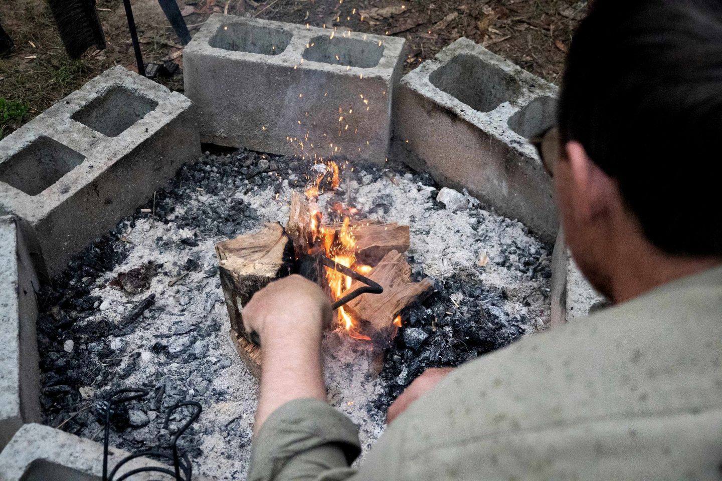 A person tending to a fire in a concrete fire pit surrounded by stone blocks.