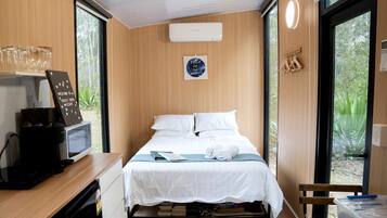 A compact room with a bed, a coffee machine, a small desk, and a window with a view of greenery.