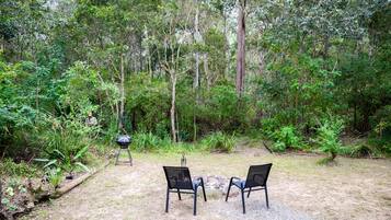 Een terras buiten met twee stoelen en een barbecue, omgeven door dicht bos.