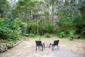 An outdoor seating area with two chairs and a barbecue grill, surrounded by dense forest. - Relaxing Tiny House Escape with Stunning Rocky Creek Views, Nestled in the Foothills of the Bauple Mountains in Glenwood, New South Wales (Glenwood)