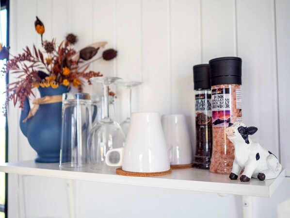 A shelf with white mugs, a glass pitcher, a blue vase with dried flowers, and salt grinders.