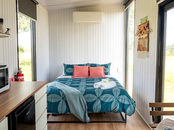 A bedroom with a bed, a bedside table, a microwave, a fire extinguisher, and a window.