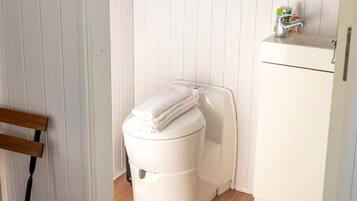 A white toilet with a towel on top, a small shelf with toiletries, and a wooden chair.