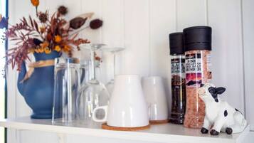 A shelf with white mugs, a glass pitcher, a blue vase with dried flowers, and salt grinders.