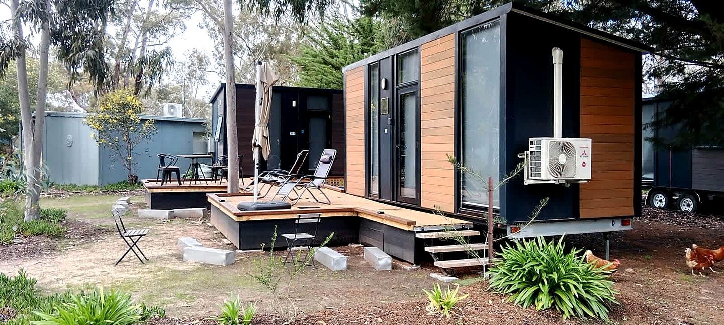 A modern, compact cabin with a deck, outdoor seating, and a large fan.