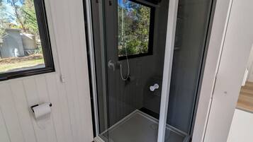 Une douche en verre avec une fenêtre, un porte-rouleau de papier toilette et une vue sur la verdure à l’extérieur.