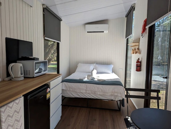 Una habitación funcional con cama, una kitchenette pequeña, microondas, hervidor de agua y ventana con vistas.