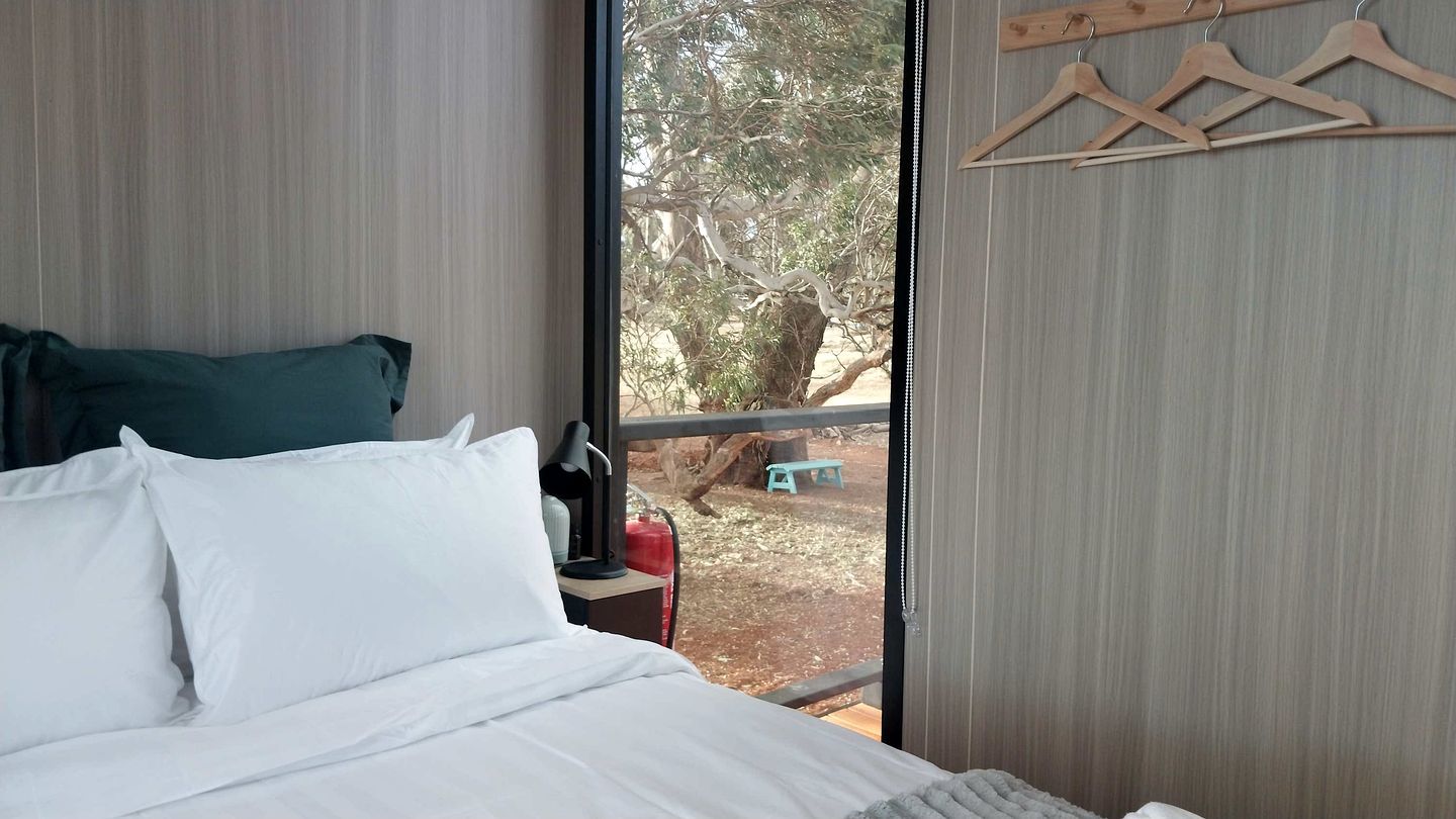 A bedroom with a bed, a window, and a wooden hanger rack.