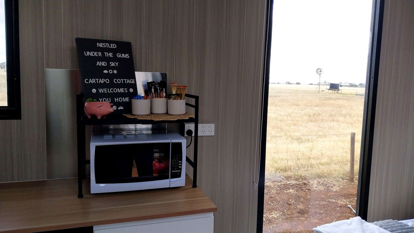 Quarto com vista para um campo, placa com texto, micro-ondas e prateleira com objetos.