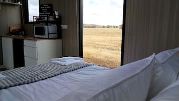 A bedroom with a bed, a desk with a computer, and a view of a field through a window.