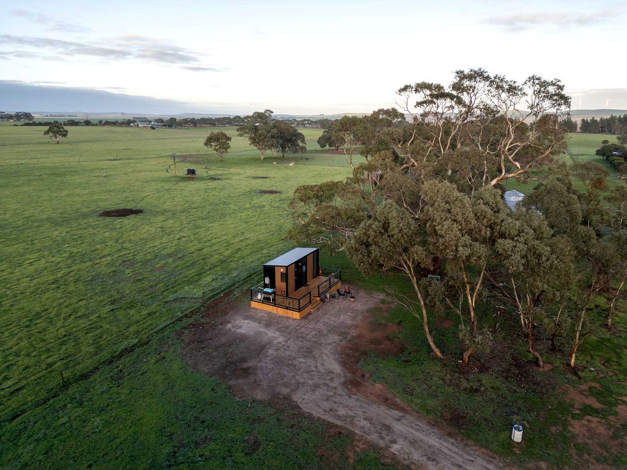 A remote cabin with a dirt path leading to it, surrounded by open fields and trees.