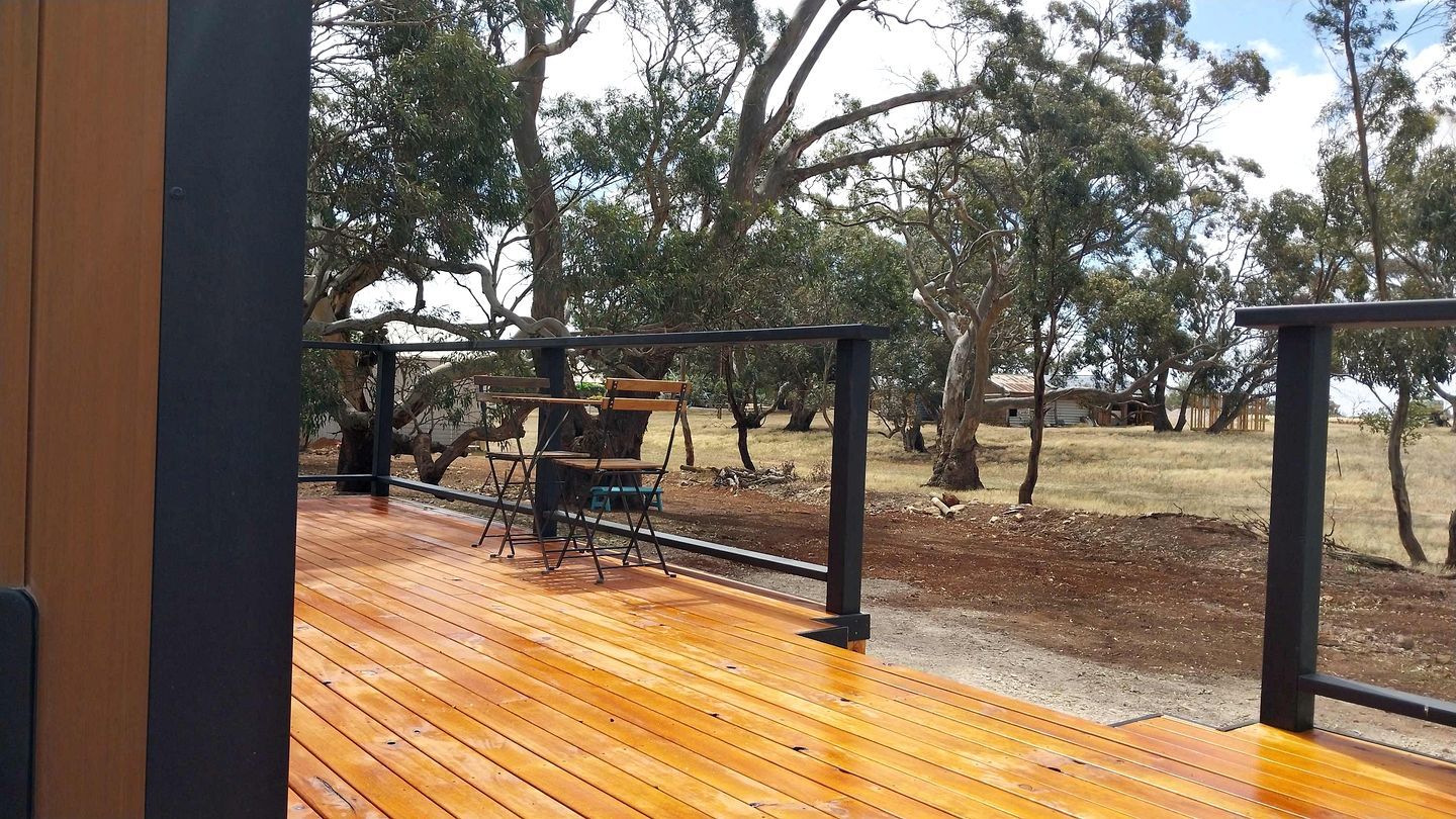 A wooden deck with a metal railing, a folding chair, and a bench.