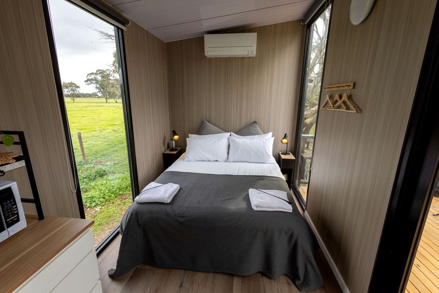 Een slaapkamer met een bed, nachtkastjes, een raam en uitzicht op de natuur.