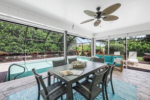 A covered outdoor area with a pool, dining table, chairs, and a ceiling fan. - Private Inland Home | Heated Pool & Near Goodland (Marco Island)