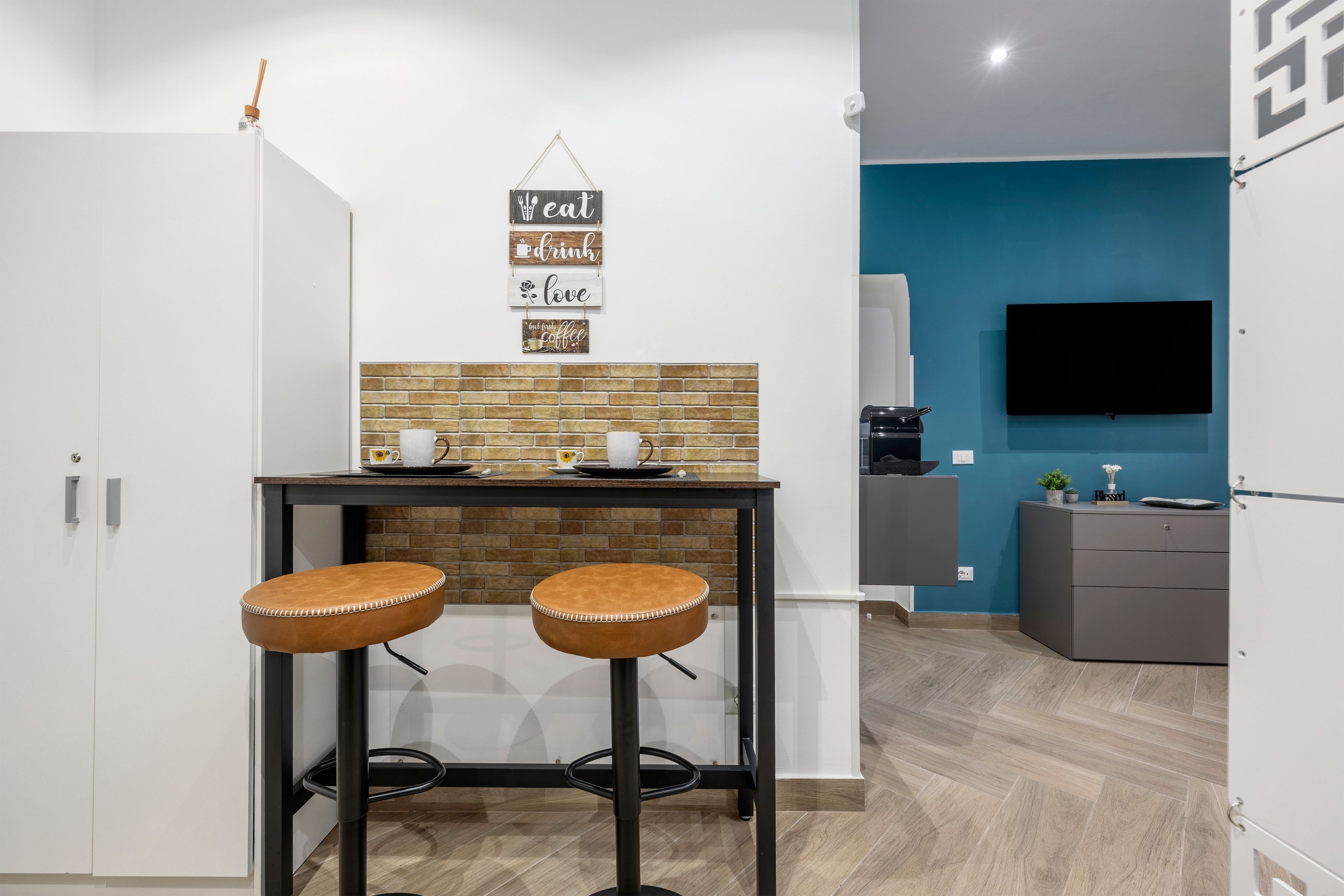 Une cuisine compacte avec un mur de fond en briques, une machine à café et un téléviseur fixé au mur.