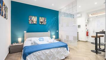 A modern hotel room with a teal accent wall, a bed with white bedding, a blue throw, and two wall-mounted paintings.