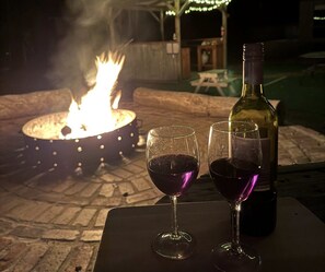 Una mesa con dos copas de vino y una botella, un hogar a leña y una piscina al fondo.
