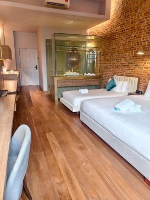 Ein Hotelzimmer mit Backsteinwand, einem gläsernen Badezimmer, Holzboden und einem Bett mit Kissen.