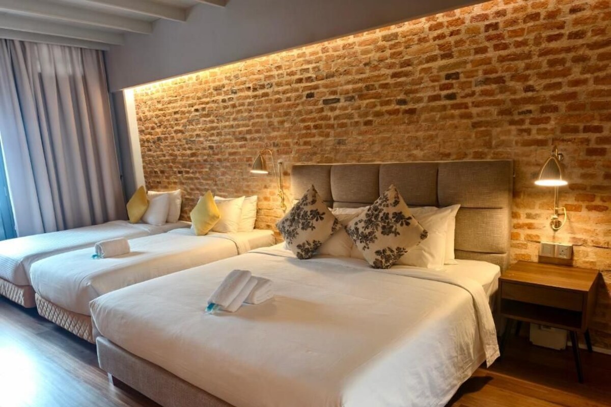 Ein Hotelzimmer mit Backsteinwand, zwei Betten mit weißen Laken und Nachttischlampen.