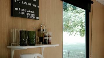 Een moderne kamer met een houten wand, een welkomstbord, een koffiezetapparaat, een waterkoker en uitzicht op groen.