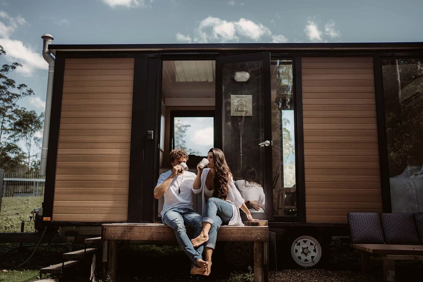 Een stel dat op een bankje zit voor een houten chalet met een glazen deur en een klein tafeltje.