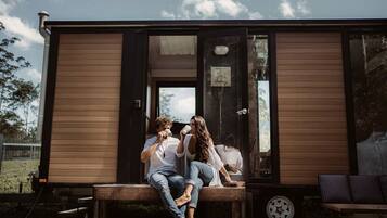 Een stel dat op een bankje zit voor een houten chalet met een glazen deur en een klein tafeltje.