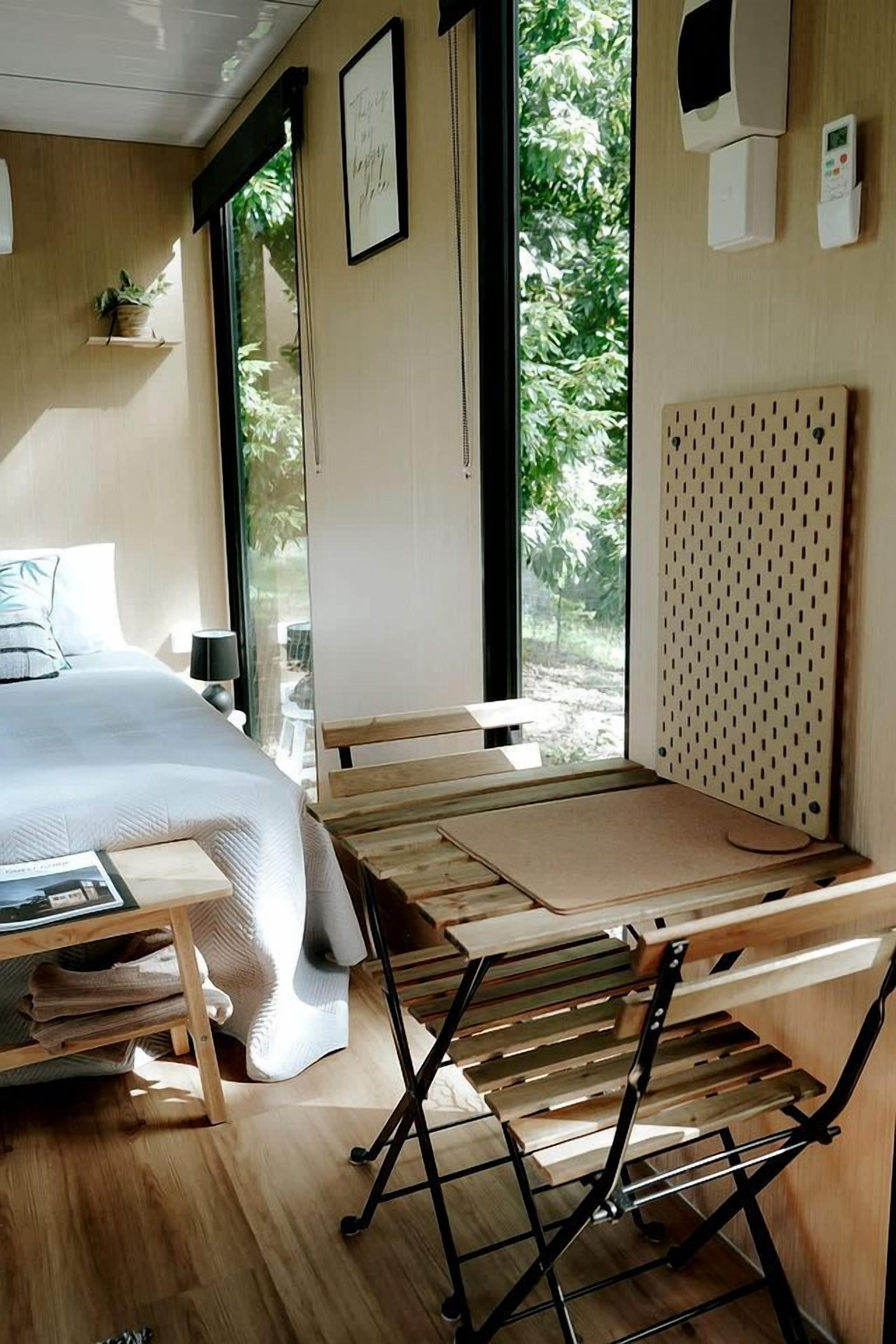 Une pièce avec un lit, une table en bois et un banc. Il y a une fenêtre donnant sur un paysage verdoyant.