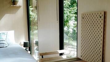 Une pièce avec un lit, une table en bois et un banc. Il y a une fenêtre donnant sur un paysage verdoyant.