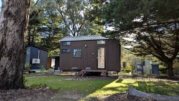 A small, single-story cabin with a metal roof, surrounded by trees and a grassy yard.