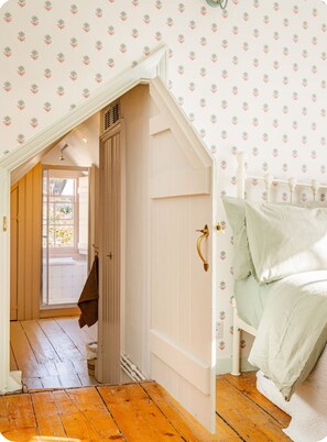 Une chambre avec un plafond en pente, un plancher en bois, un lit avec une literie blanche et une porte donnant sur un couloir.