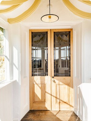 Une porte à deux battants en bois, dotée de panneaux de verre et surmontée d’un luminaire.