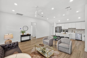 A spacious living area with a sofa, armchairs, and a coffee table. A kitchen with white cabinets and stainless steel appliances is visible in the background. - Brand New, Minimalist and Spacious 4BR Retreat (Abilene)