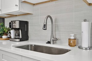 A modern kitchen with a stainless steel sink, a coffee maker, and a bottle of hand soap.