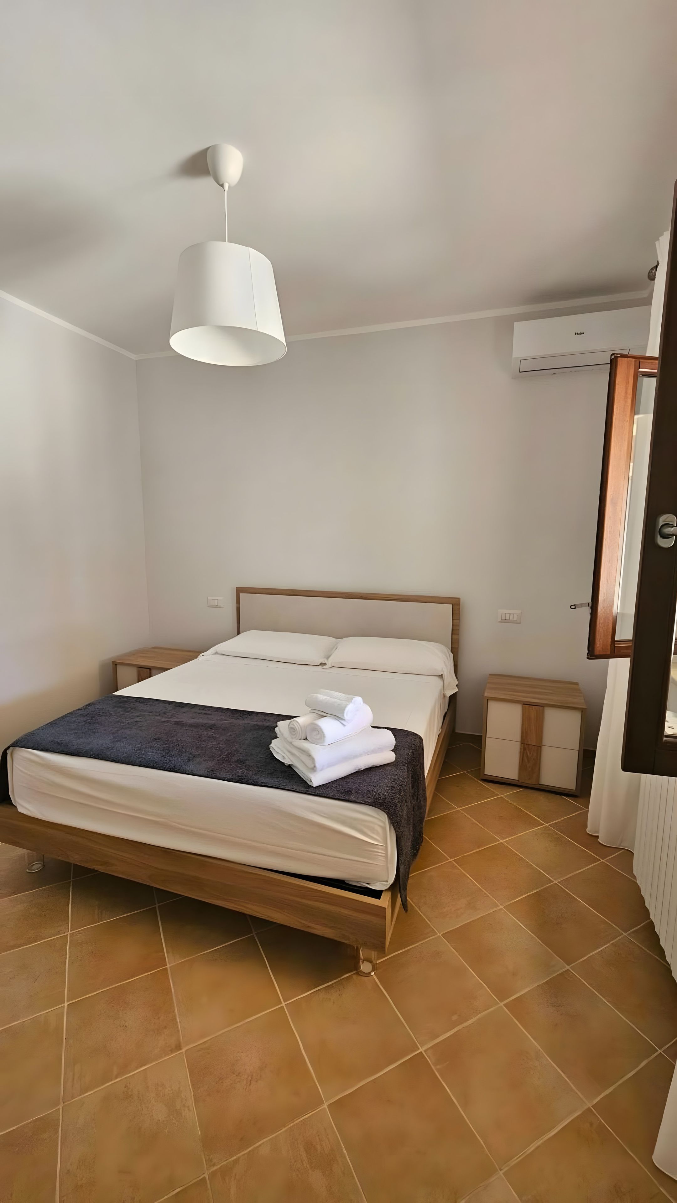 Un dormitorio con cama, mesita de noche, lámpara colgante y unidad de aire acondicionado.