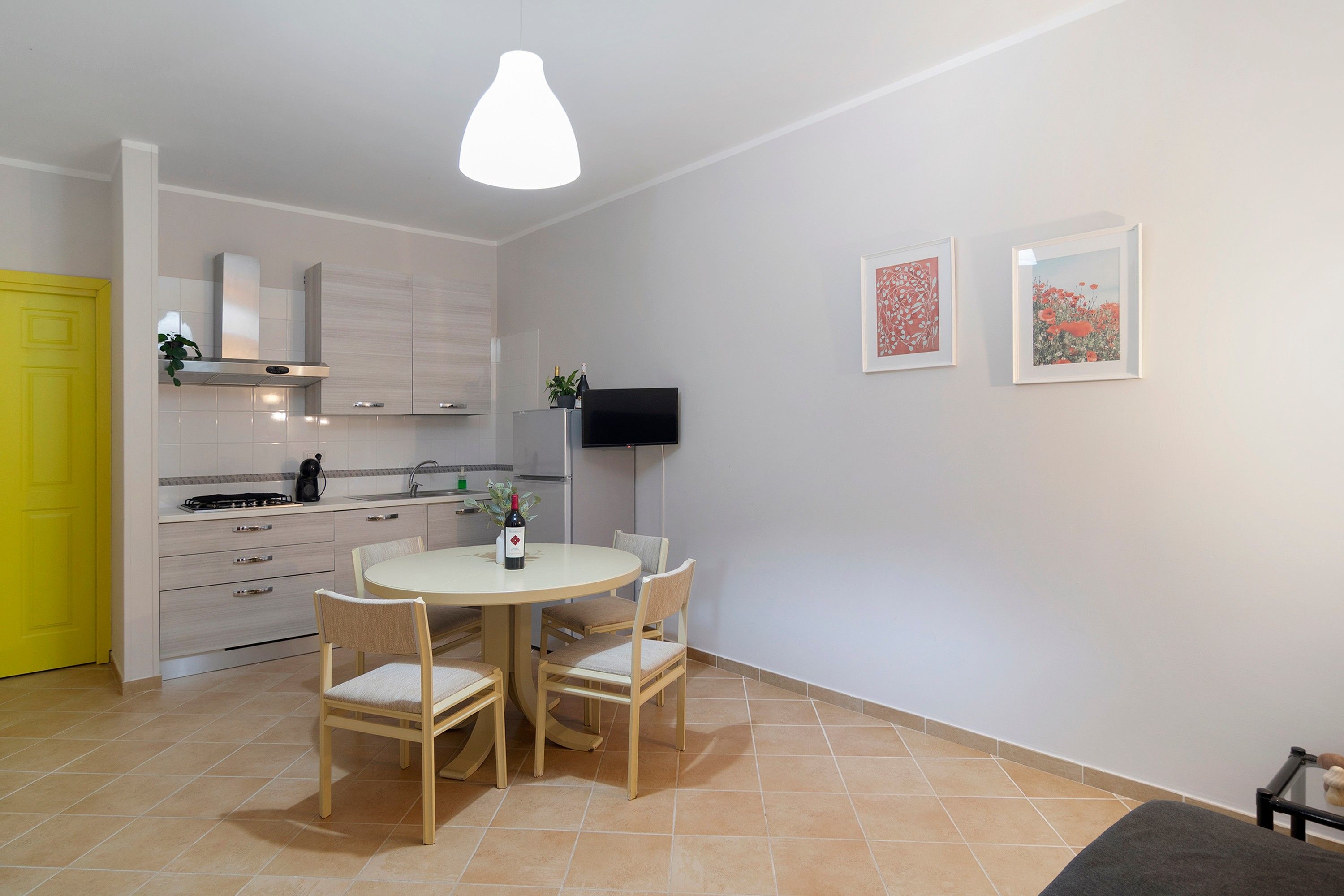 A modern kitchen with a dining area, a yellow door, and two framed artworks on the wall.